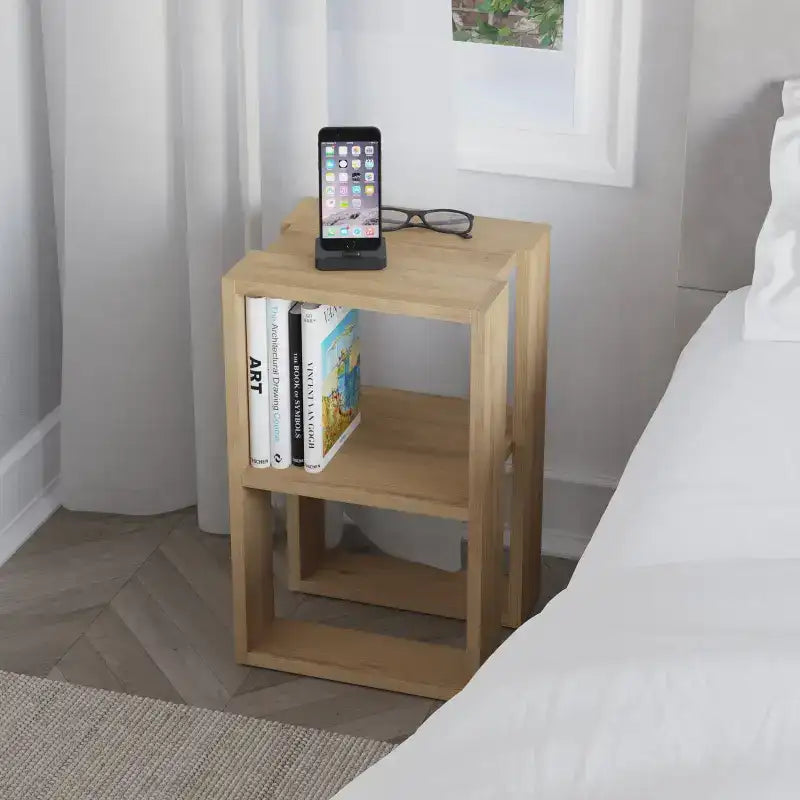 Light oak bedside table with open shelves holding books and a smartphone on top.