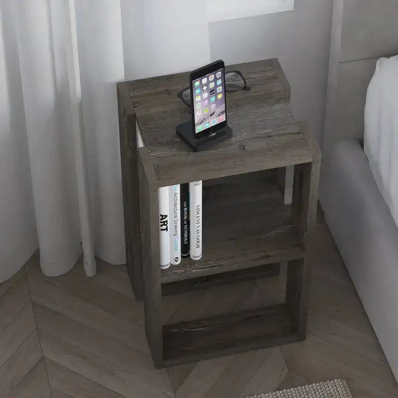 Dark wood bedside table with open shelves holding books and a smartphone on top.