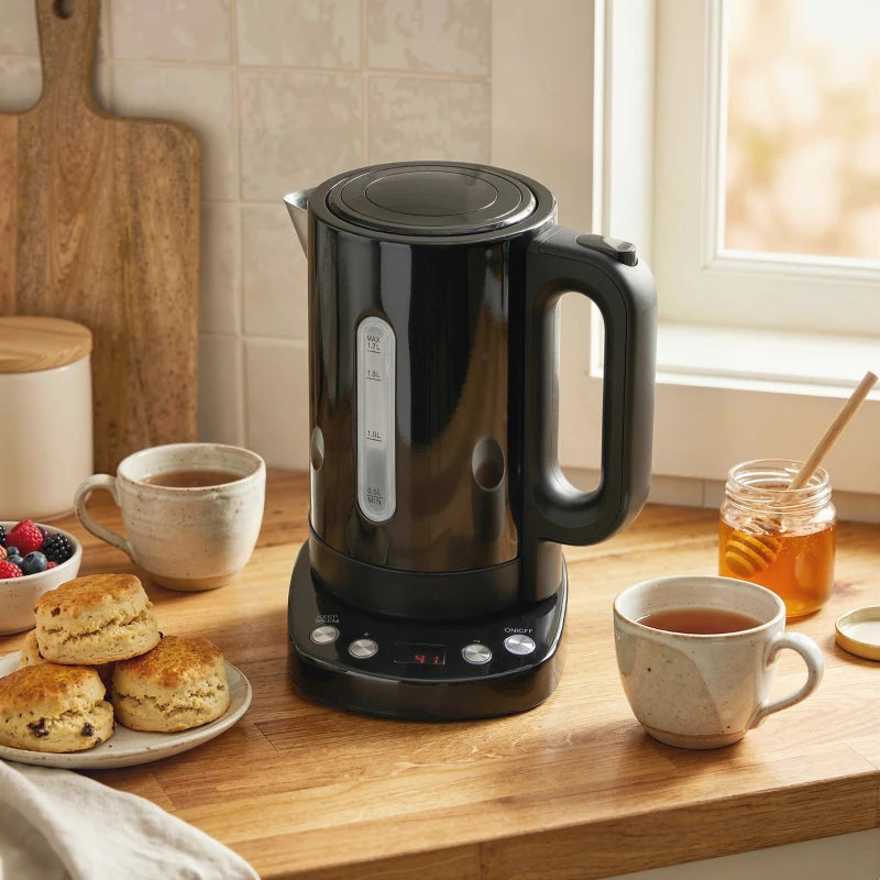 Black electric kettle on countertop near cups and fruit, with side handle