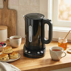 Black electric kettle on countertop near cups and fruit, with side handle