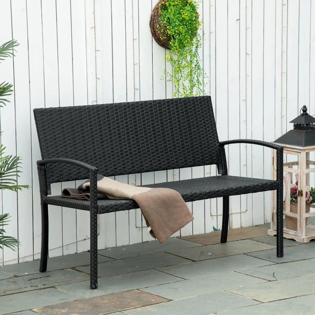 Black woven outdoor loveseat with armrests and a beige throw draped over the seat
