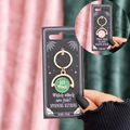 Keyring with 'Bad Witch' design on a black card, held by a hand against a pink curtain.