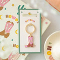 Pink cowboy boot keyring with gold-tone ring and charm, on retail card