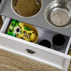Open white storage drawer with kibble and treats beside stainless steel bowls