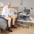 Black commode chair with padded seat and caster wheels beside bed