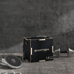 Black wooden jump box on gym floor, with barbell plates beside it