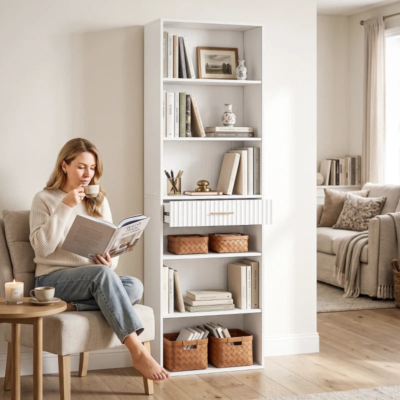 White tall narrow bookcase with open shelves and drawer, viewed in room