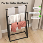 Black steel towel rack with three bars, holding white towels and an orange cloth.