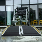 Wheelchair on black threshold ramp with non-slip surface, yellow edge stripes, and end plates