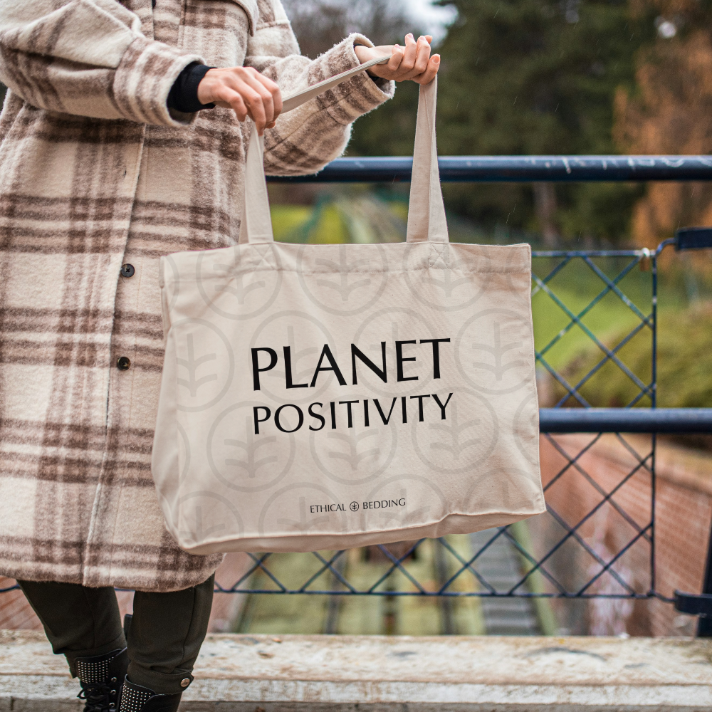 Person holding a tote bag with 'Planet Positivity' text, standing outdoors.