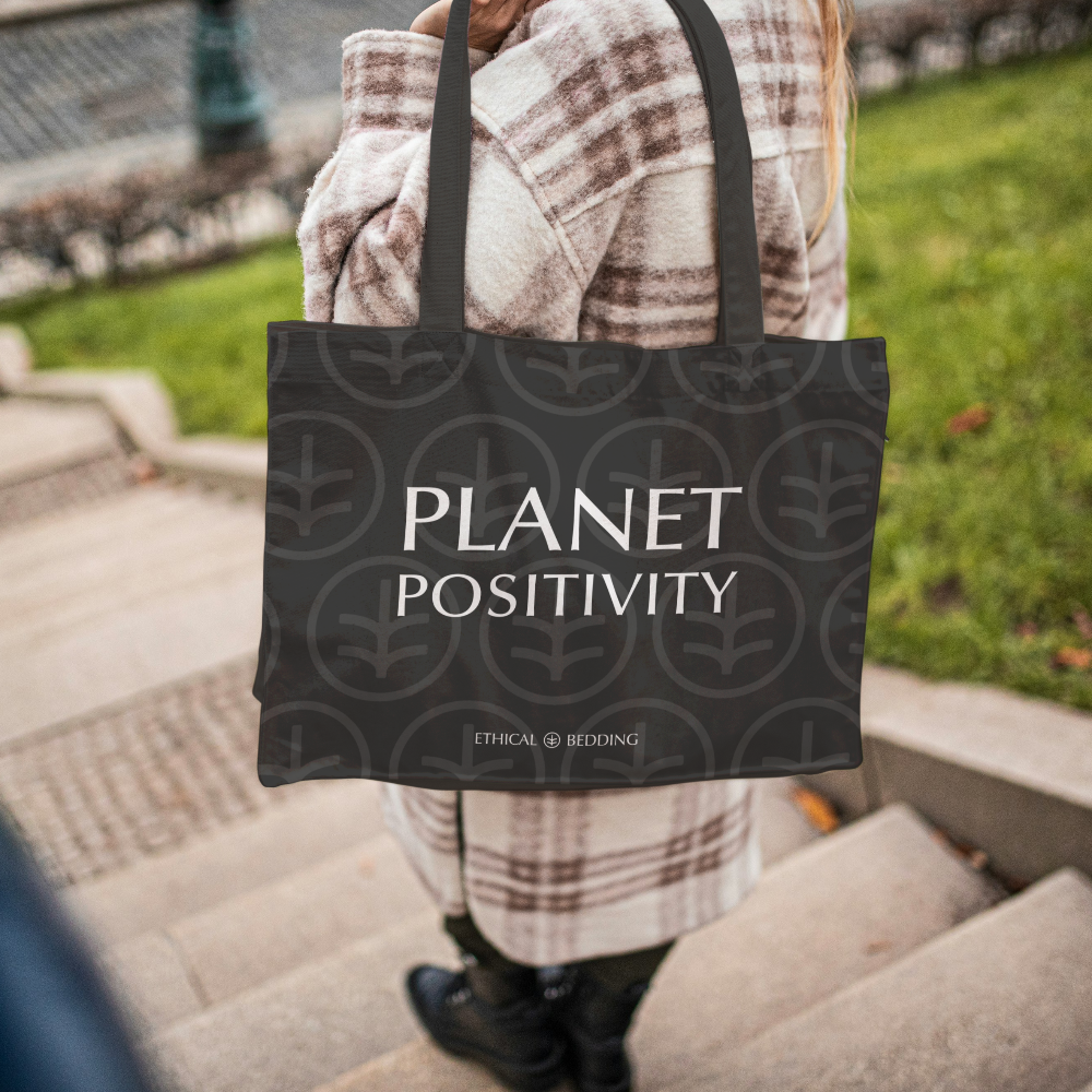 Person holding a tote bag with 'Planet Positivity' text outdoors.