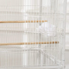 White bird cage interior with wooden perch and hanging feeder cup