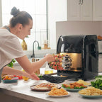 Black air fryer oven with food trays on counter as someone loads the basket