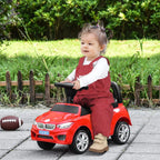 Red ride-on car walker toy with black steering and seat, child seated on outdoor pavement