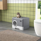 Grey enclosed cat litter box with lid and circular front entry; cat perched on top
