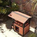Outdoor cat house with roof and front door, dark legs and brown wood walls on patio