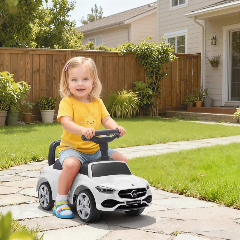 White ride-on car walker with black seat and steering wheel, outdoors on driveway