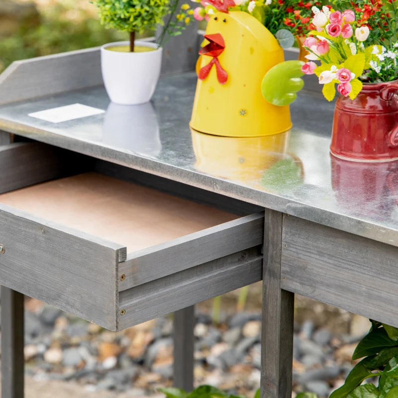 Grey potting table with raised metal edge and drawer opening, with potted plants