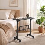 Black overbed table with top surface, lower shelf, and caster wheels in a bedroom