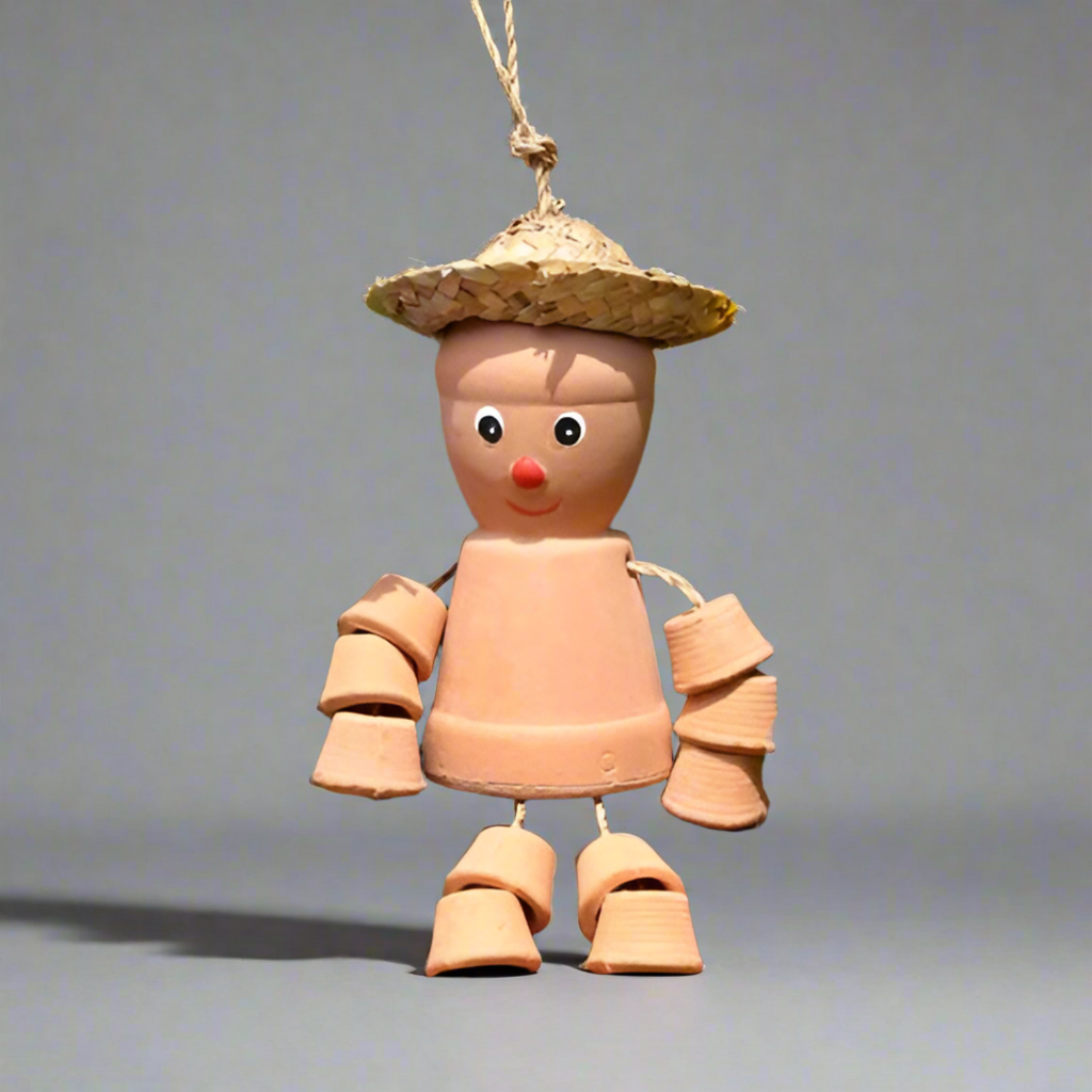 Terracotta scarecrow decoration with a straw hat among colorful flowers