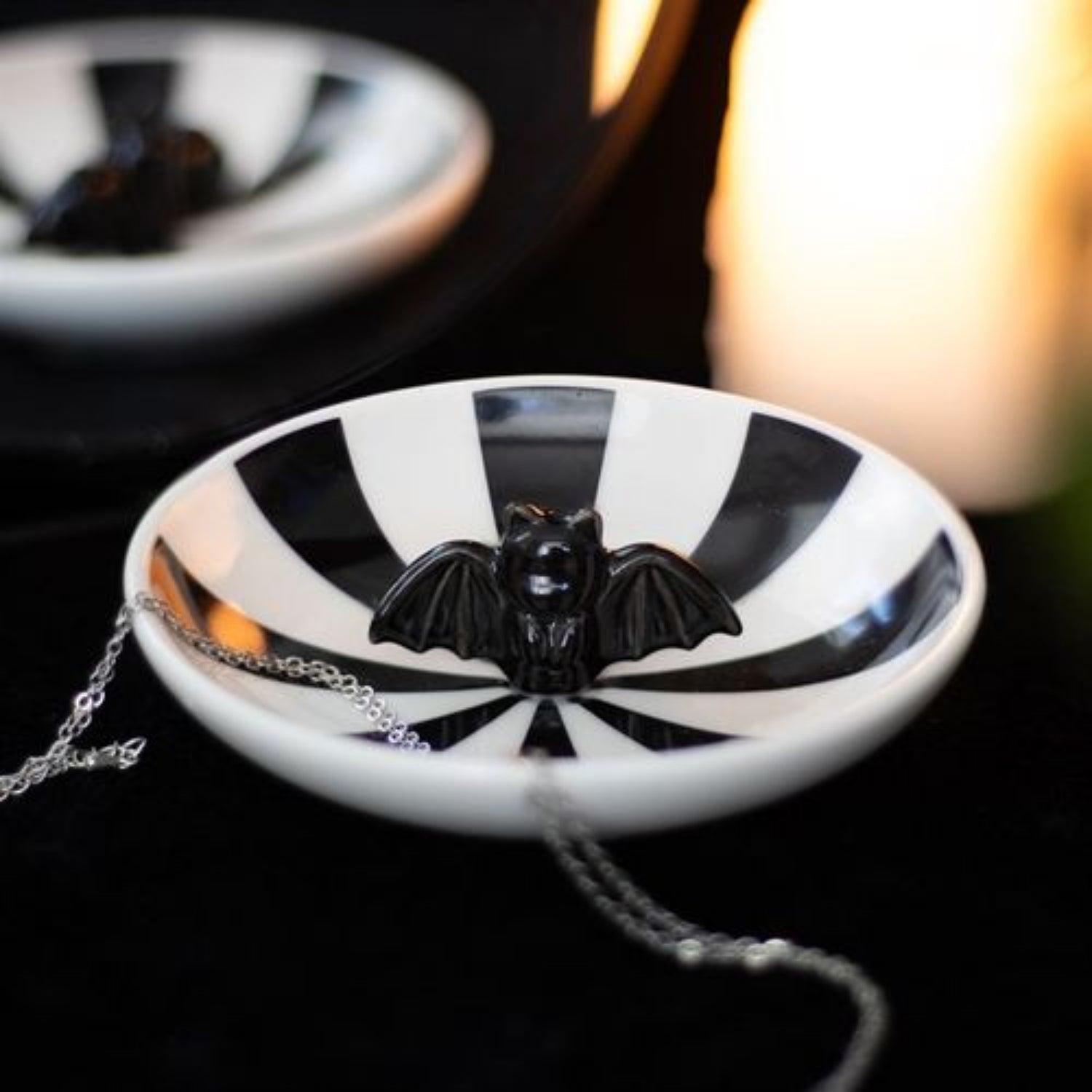 Black bat pendant on a necklace against a black and white striped background