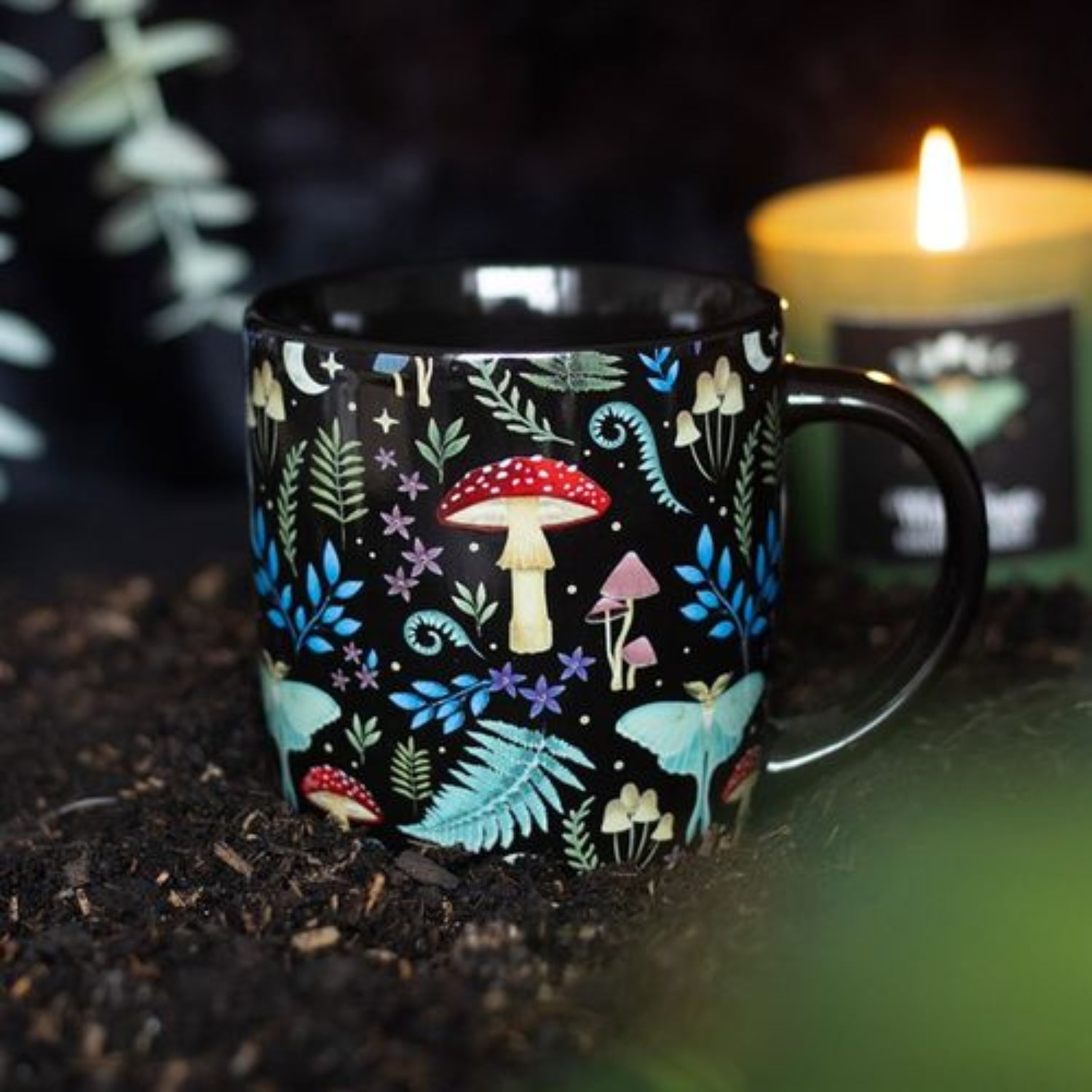 Black mug with colorful forest pattern on a dark surface with a candle in the background