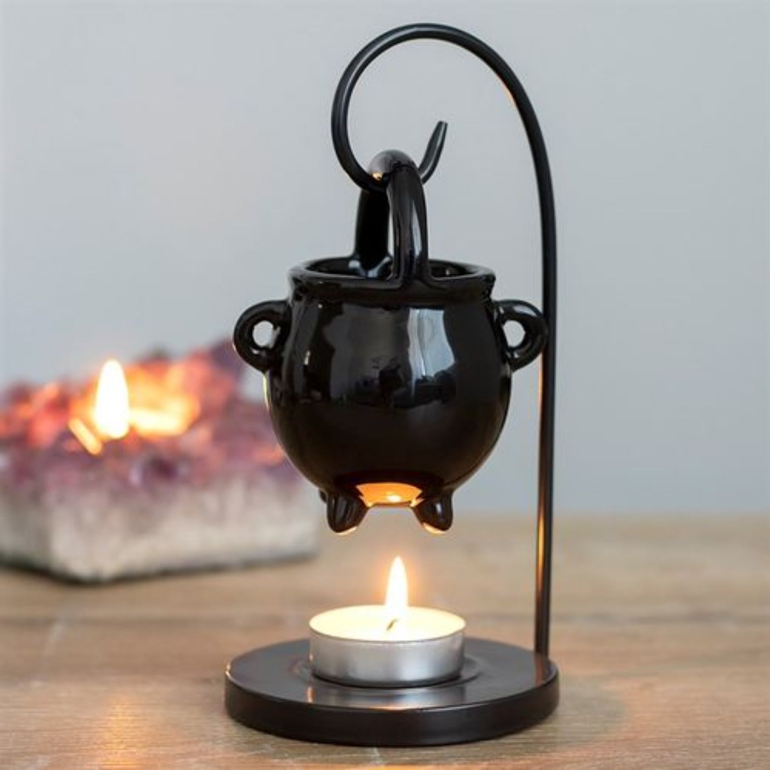 Black cauldron-shaped oil burner with a lit candle on a wooden surface.