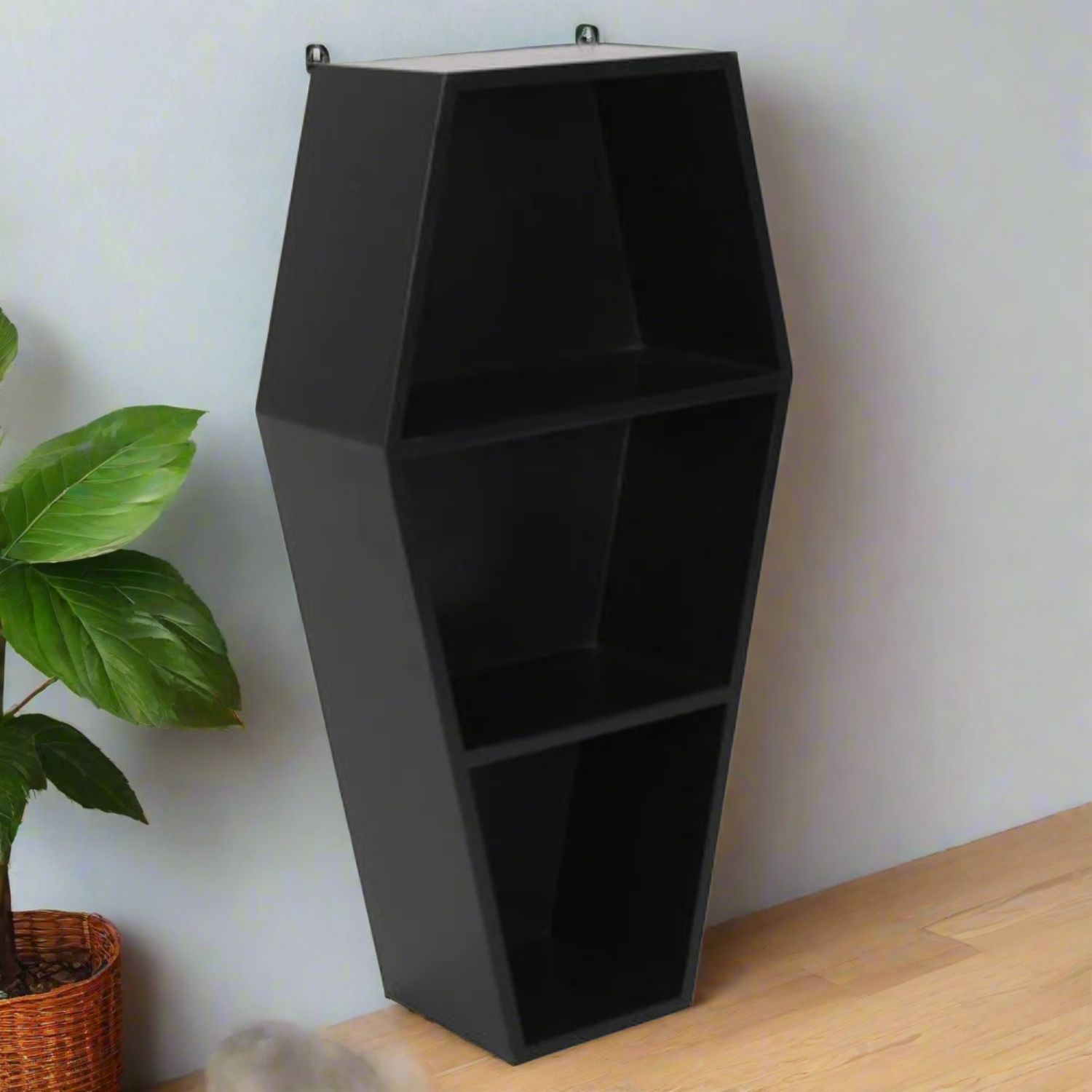 Black hexagonal shelf against a white wall with a plant on a wooden floor.