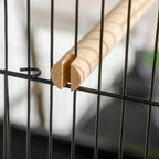 Wooden perch attached across black wire bars inside bird cage