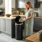 Black automatic trash can with lid open in kitchen while disposing food scraps