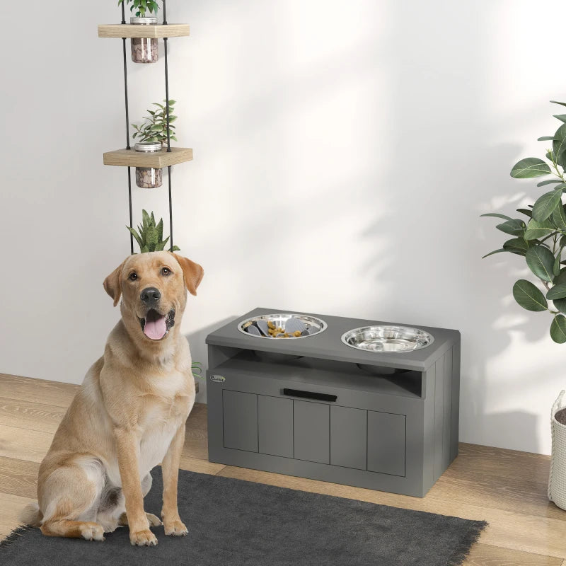Grey raised dog feeding station with two stainless bowls and a dog seated nearby