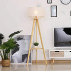 Tripod floor lamp with cream fabric shade and round storage shelf on wooden legs