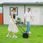 Black outdoor lawn grass roller with push handle and round drum on green turf