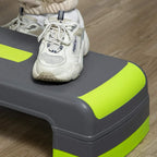 Grey and green aerobic step with green traction pads under athletic shoes.
