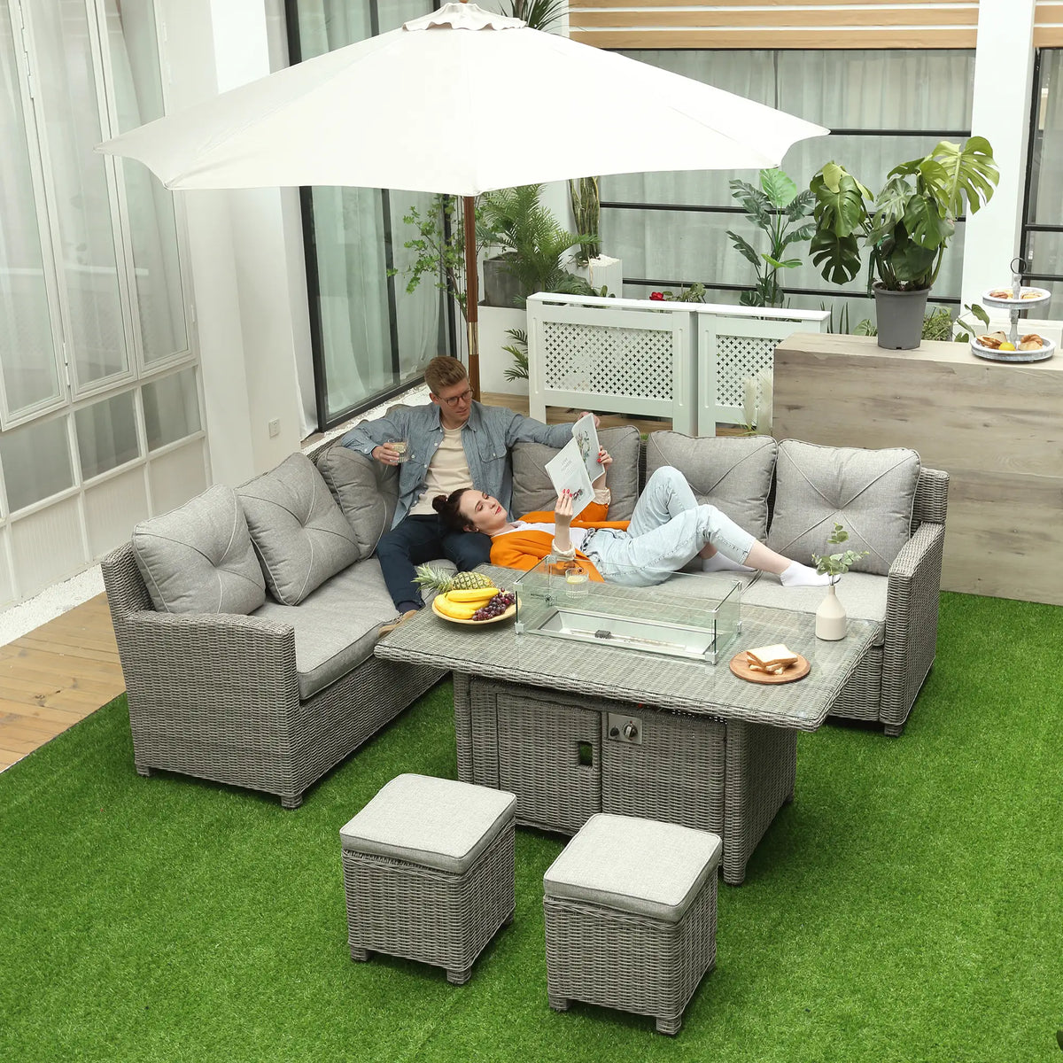 Grey L-shaped rattan sofa set with glass-top fire pit table and two footstools