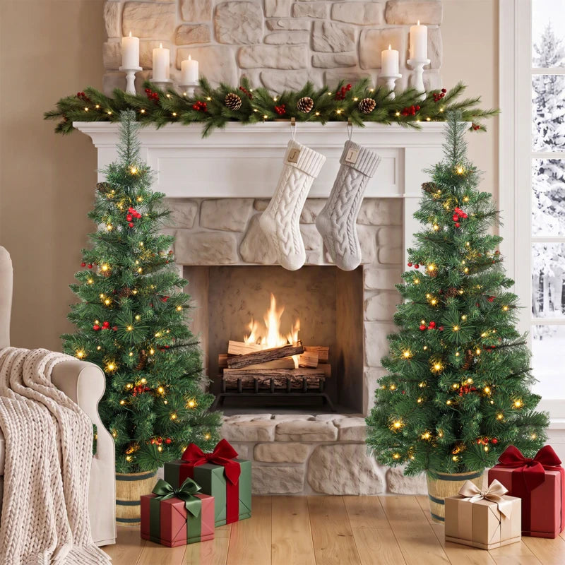 Two prelit Christmas trees in pots with green needles, pinecones, berries, and warm LED lights