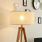 Cream fabric drum shade on a natural wood tripod floor lamp with warm light