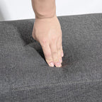 Grey upholstered bench ottoman cushion pressed by a hand, showing padding