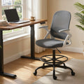 Grey mesh office chair with flip-up armrests, positioned by a desk and window.