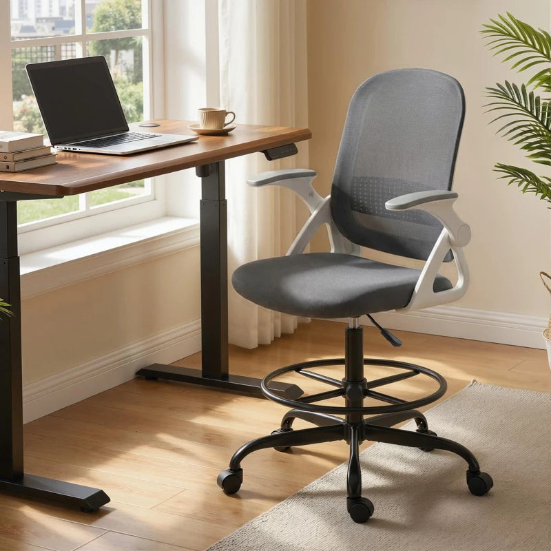 Grey mesh office chair with flip-up armrests, positioned by a desk and window.