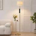 Gold-tone floor lamp with linen shade and small side shelf on round base