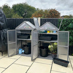 Grey cold frame greenhouse with double doors open, holding pots and garden tools